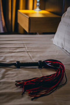 Leather flogger laid out on sheet near bedside table lamp