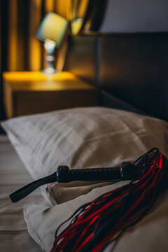 Leather flogger positioned on pillow near bedside lamp and nightstand