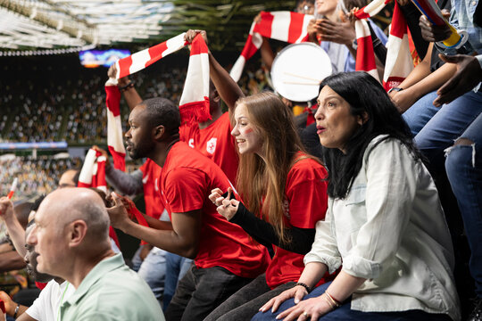 Focused football supporters watching dramatic final minutes of a soccer match filled with suspense and tension. Sports fans asking for the final whistle in the stadium, speechless after close call.