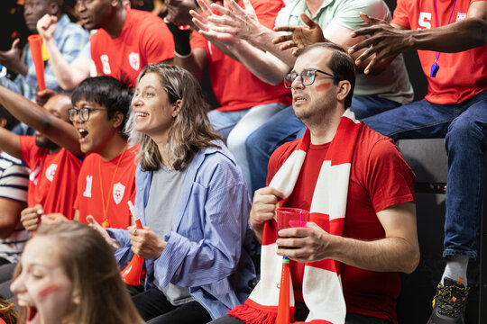 Red team football supporters showing mixed reactions in crowded stadium stands during tense live soccer match. Inclusive sports fans clenching fists speechless after near goal opportunity.