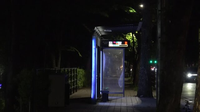 Empty illuminated bus stop at night with passing car traffic on the side, 4K