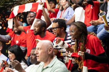 Female soccer fans celebrating goal with raised arms in crowded stadium stands, red team supporters and energetic live match atmosphere in fan section. Supporters remain nervous. © DC Studio