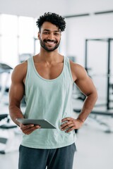 Fototapeta premium Man holding tablet and smiling in bright gym interior