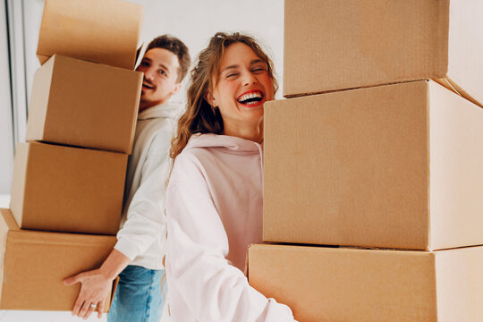 Moving to a new apartment concept. Young couple holding stack of cardboard boxes. Happy laughing guy and girl carrying household items.