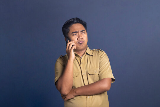 Indonesian civil servant man frowning while talking on smartphone with serious skeptical expression