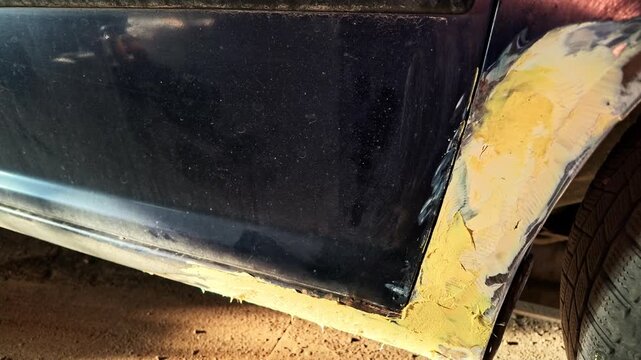 Body filler applying process on a damaged car fender in a professional garage