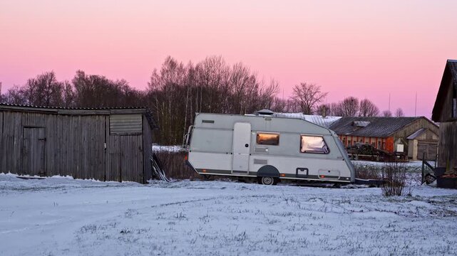 Recreational vehicle with warm light inside sitting in a winter countryside at dusk