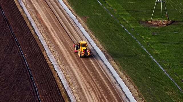 Road grader compacting a new dirt road between agricultural fields aerial view