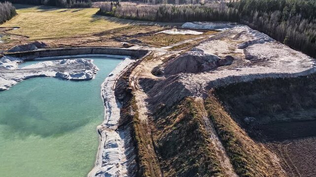 Drone footage of an open pit mine with sand heaps and a green artificial lake