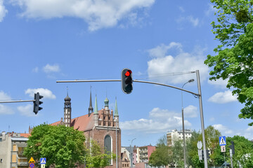A red traffic light hanging over an urban street, with a historic brick church in the background against a blue sky. Ideal for city transportation, traffic regulation, and travel concepts  © Яна Руднева