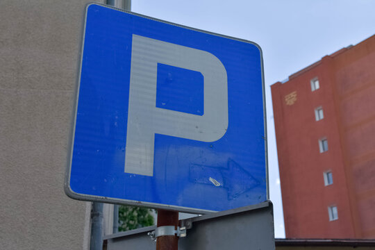 A blue public parking sign on a metal post with a red building in the background. Great for city parking rules, urban infrastructure, and traffic regulation concepts 