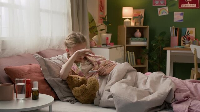 Sick gen alpha child removing thermometer and reading number, then raising hand to her forehead and coughing when lying in bed