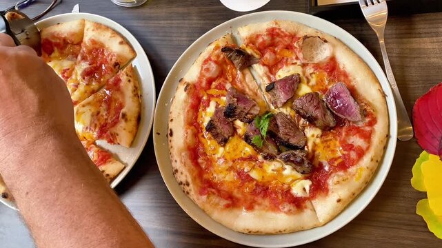  Top view of fresh gourmet pizzas on a restaurant table with a hand cutting slices.
