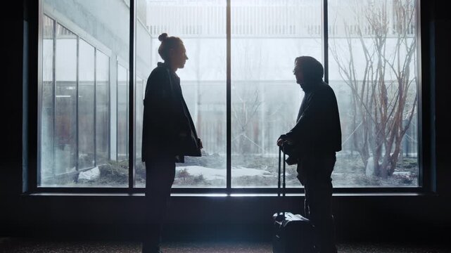 Two silhouetted figures exchange a suitcase for an envelope filled with money in front of a large window