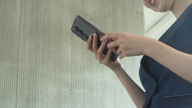 Close-up of woman using smartphone indoors, modern lifestyle and mobile communication concept with copy space on textured wall background.