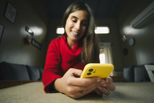 Ultra wide-angle close-up of a young Hispanic woman using her smartphone at home. Modern technology and digital lifestyle concept.