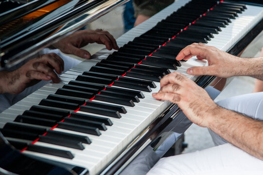 Primo piano delle mani di un pianista che suona un pianoforte. Le mani sono posizionate sui tasti bianchi e neri. Il pianoforte riflette le dita del pianista e la tastiera.