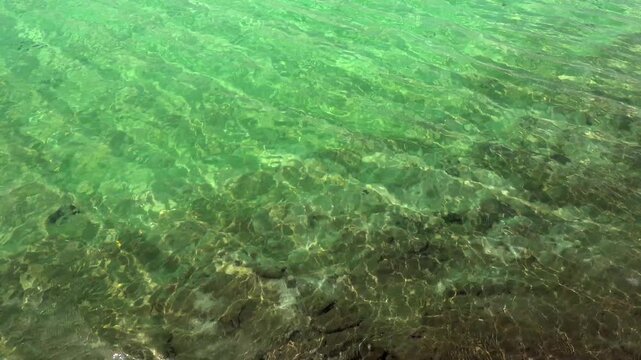 Overhead static shot of emerald green water ripples with sun reflections over rocks, clear transparent lake background