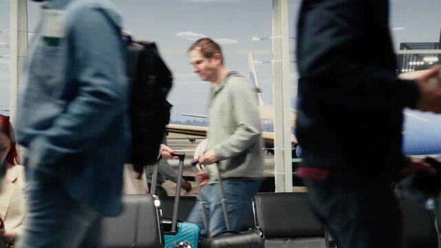 Blurred passengers and travel documents move through the foreground of an airport terminal, with seating, aircraft windows and a runway view behind them.