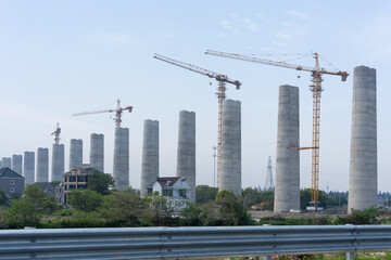 Fototapeta premium massive concrete bridge piers and yellow tower cranes at highway construction site
