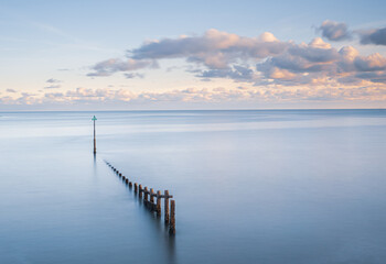 Fototapeta premium Minimalist Long Exposure Seascape with Wooden Posts and Calm pastel Water 