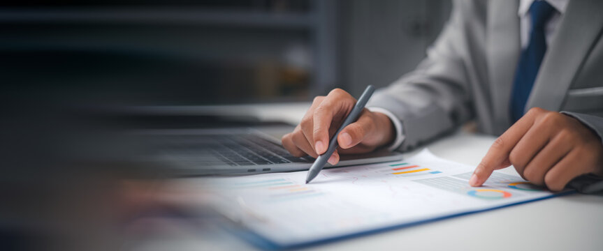 Businessman analyzing financial graph report and marketing data on clipboard with laptop. Investment planning, data analytics, and corporate strategy concept with copy space for text.