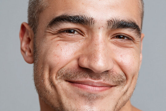 Smiling man portrait with cheek illuminated by soft daylight, close up face showing skin texture, stubble, freckle and warm expression