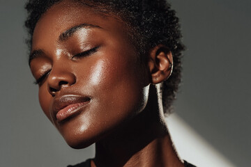 Obraz premium Radiant dark skinned woman with closed eyes and glowing skin in soft studio light, serene expression and textured short hair conveying calm confidence