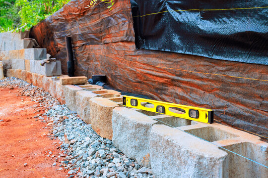 Workers are building retaining stone wall using concrete blocks checking level of structure with tool.