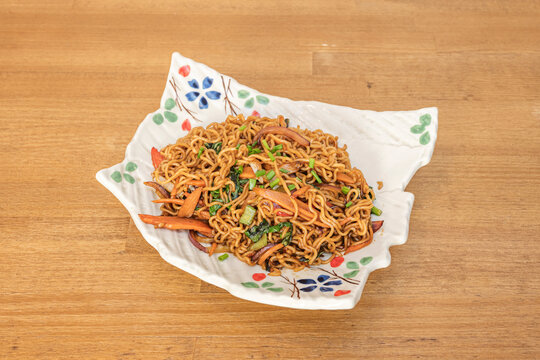 A low angle shot captures wide rice noodles (ho fun) stir-fried with oyster sauce, beef, green bell pepper, onion, and bean sprouts, served in a deep gray ceramic bowl.