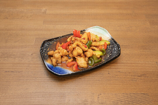 A Chinese recipe for sweet and sour stewed chicken with vegetables and sauce on a black porcelain tray