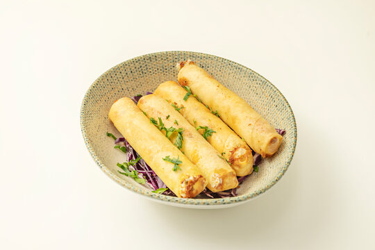 A close-up of four rice paper rolls cut in half diagonally, revealing the geometric layers of lettuce, mint, rice noodles, and prawns, on a light wooden table.