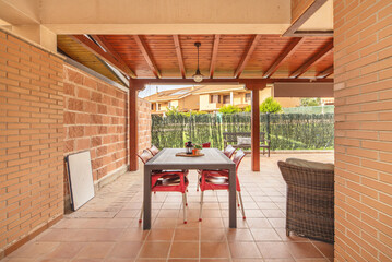 Fototapeta premium A modern terrace with a polished cement floor, an aluminum pergola, a portable barbecue, and a corner with aromatic plants in ceramic pots.