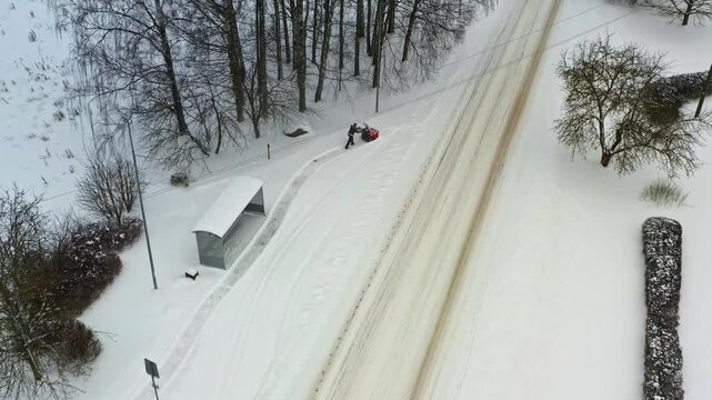 Utility worker cleaning a snowy pavement with a snow thrower machine after a winter blizzard