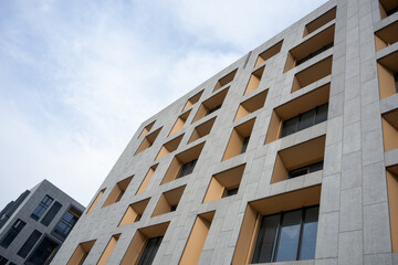Fototapeta premium Modern building facade featuring geometric windows and stone texture against blue sky