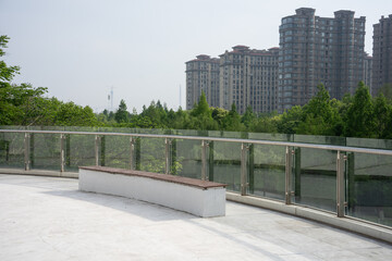 Modern glass railing and bench on a rooftop terrace with high-rise buildings in the background © zhu difeng