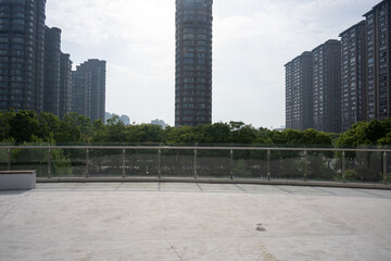 Fototapeta premium Spacious rooftop terrace with glass railing overlooking modern high-rise residential buildings and green trees
