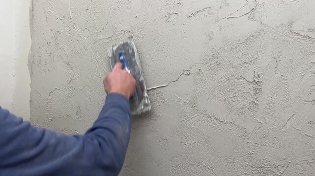 A person uses a trowel to apply a textured finish to a wall as part of a home renovation. The task takes place in a well-lit room.