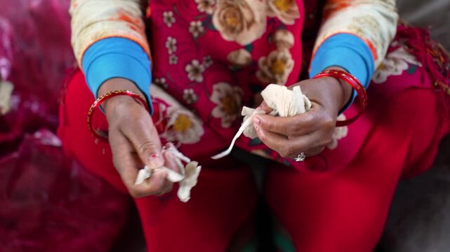 Dhangadhi, Nepal - 08 January 2024: View of a woman's hands processing white cotton fibers while wearing traditional red floral clothing and bangles.