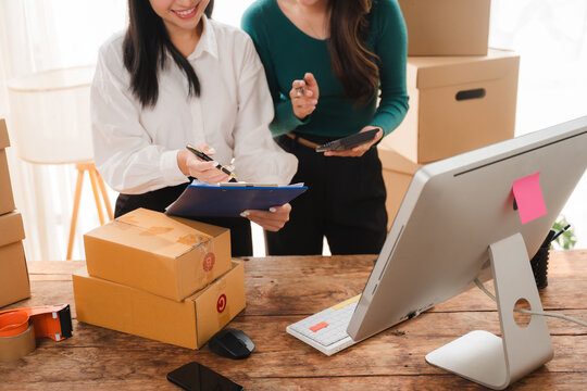 Packaging for Success: Two women work together to prepare packages for shipment, surrounded by cardboard boxes and office supplies.