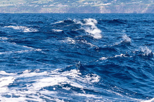 Deep blue ocean waves with white foam and distant coastline of Sao Miguel in the Azores