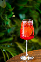 This is a vibrant red spritz cocktail with a citrus slice garnish, served in a wine glass on a...