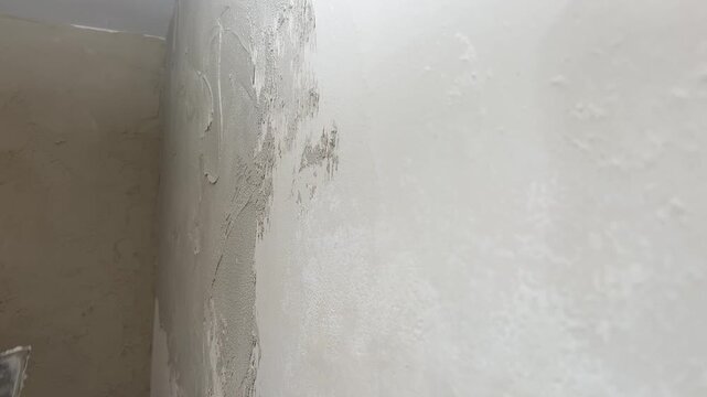 In a local home, a worker applies plaster to a wall using a trowel. The task involves smoothing the surface for a clean finish.