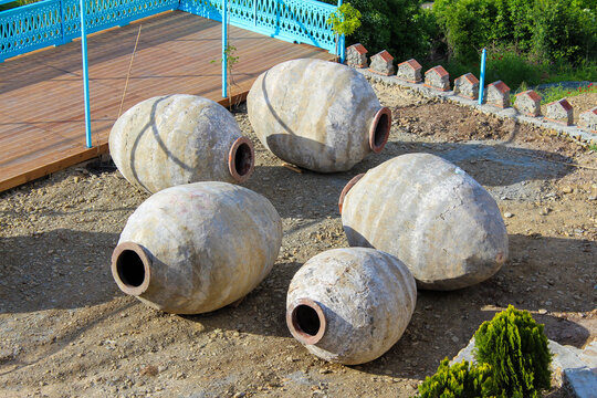 Several old Kvevri Qvevri Churi of different sizes on the grass near a stone wall. Earthenware clay vessel used for the fermentation, storage and ageing of traditional Georgian wine.
