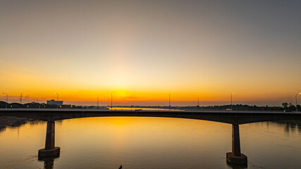Fototapeta premium Stunning aerial view of a glowing sunset over the Friendship Bridge and surrounding city skyline. Warm golden light reflects across the river, creating a dramatic yet tranquil scene travel