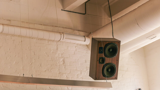 Vintage wooden speaker box suspended from ceiling with exposed pipes and brick wall