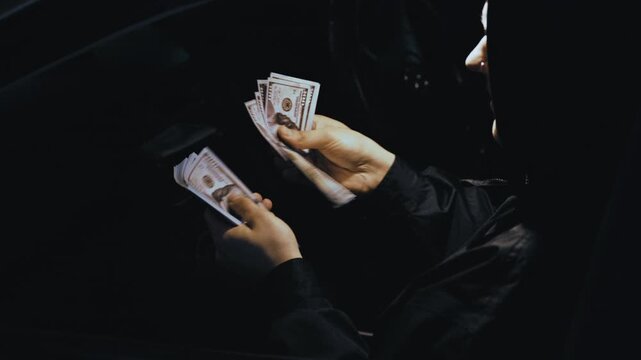 Criminal hands counting a large amount of us hundred dollar bills inside a dark car at night