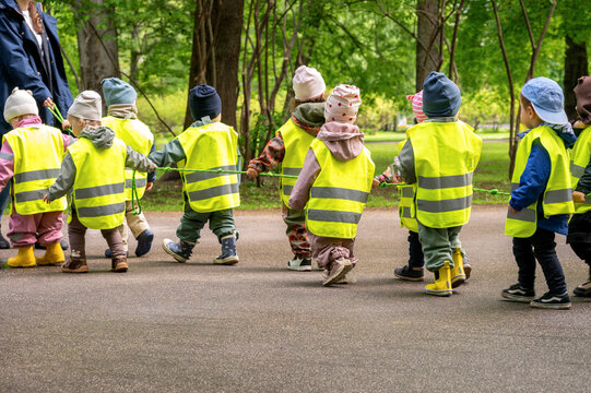 Kindergarten teacher leading a group of children in yellow safety vests walking in line with a safety rope