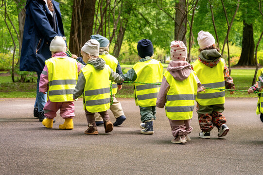 Kindergarten teacher leading a group of children in yellow safety vests on a walk, children holding a rope for safety
