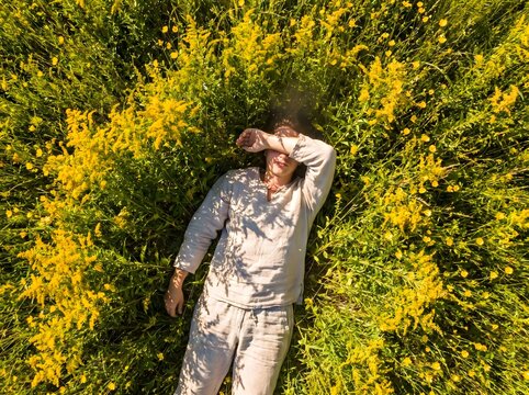 Vista a&eacute;rea cenital de una mujer acostada sola en un vasto campo de flores amarillas. Fotograf&iacute;a con dron de mujer relaj&aacute;ndose en prado primaveral concepto de escala humana
